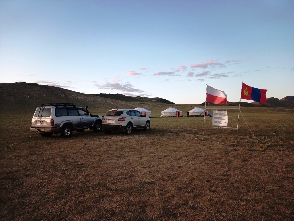 trzy namioty jurty w stepie, na pierwszym planie dwa samochody i flagi polska i mongolska