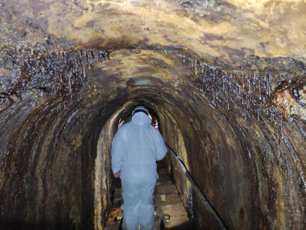 osoba w kombinezonie idąca środkiem starego tunelu w kopalni