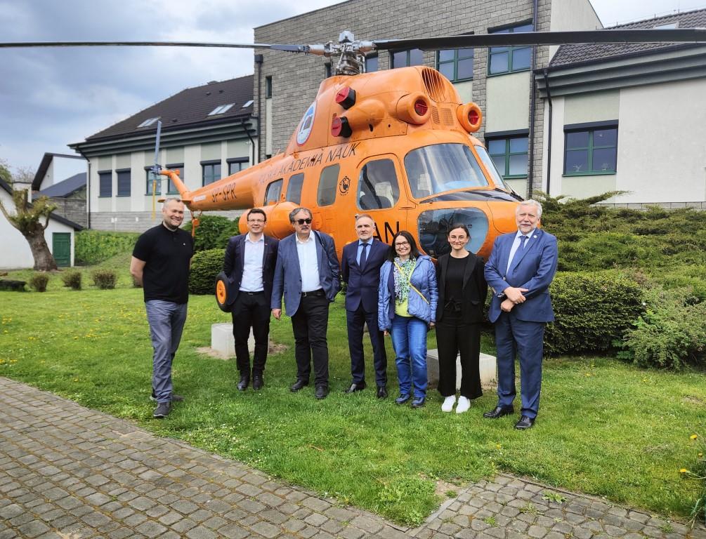grupa osób stojąca na trawie , z tyłu pomarańczowy helikopter