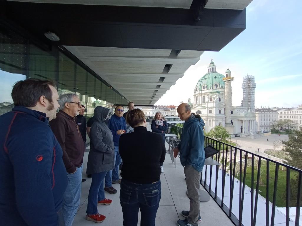 grupa ludzi stojących na tarasie budynku z widokiem na miasto Wiedeń