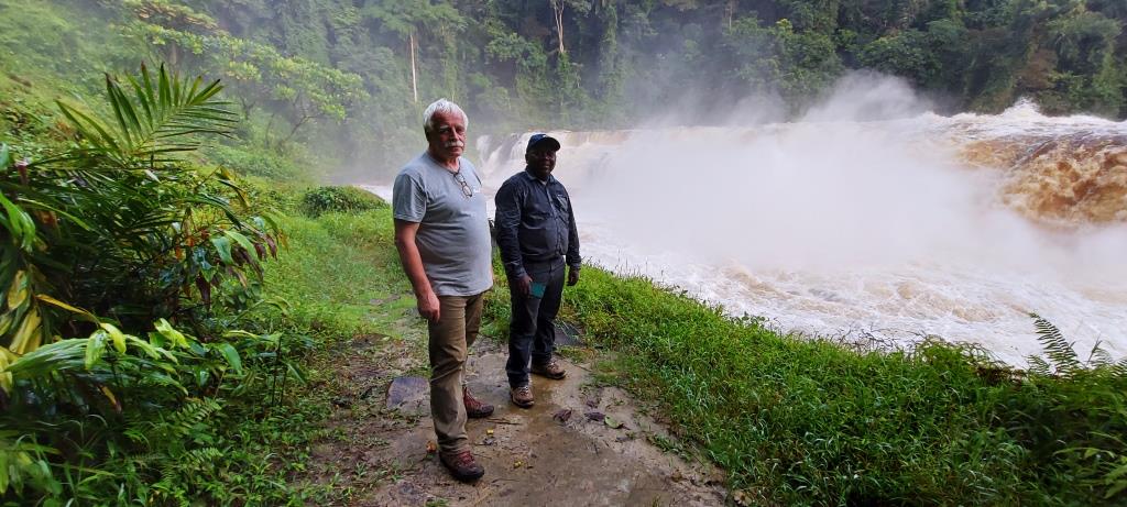 dwóch mężczyzn w terenowych strojach pozuje do zdjęcia na tle rwącej rzeki i tropikalnej przyrody
