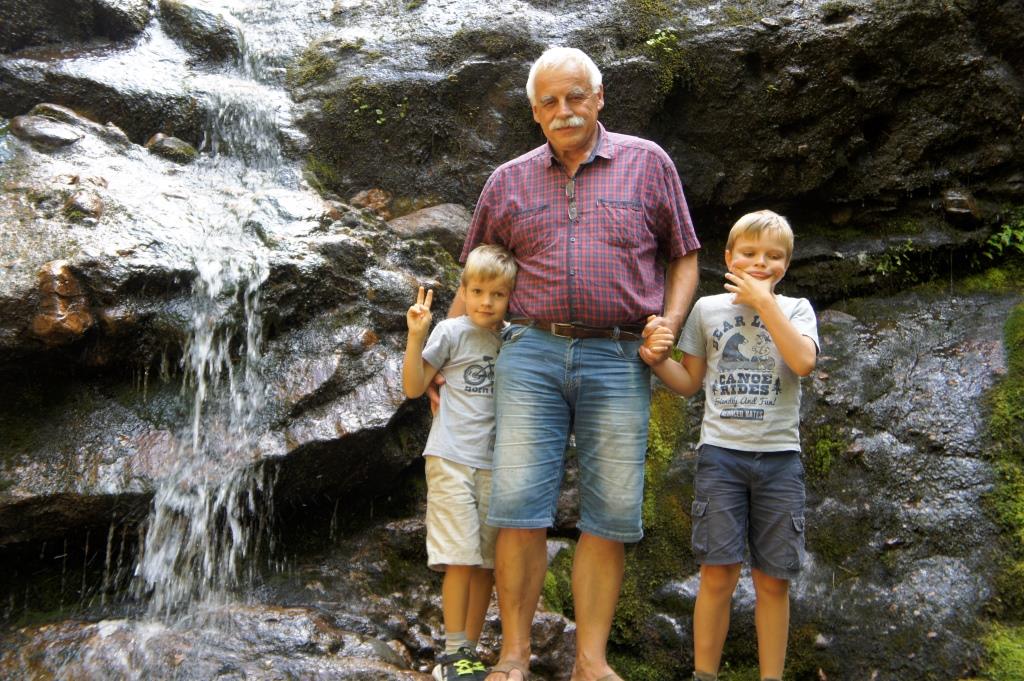 mężczyzna z dwójka chłopców pozują do zdjęcia na tle skał górskich i niewielkiego wodospadu