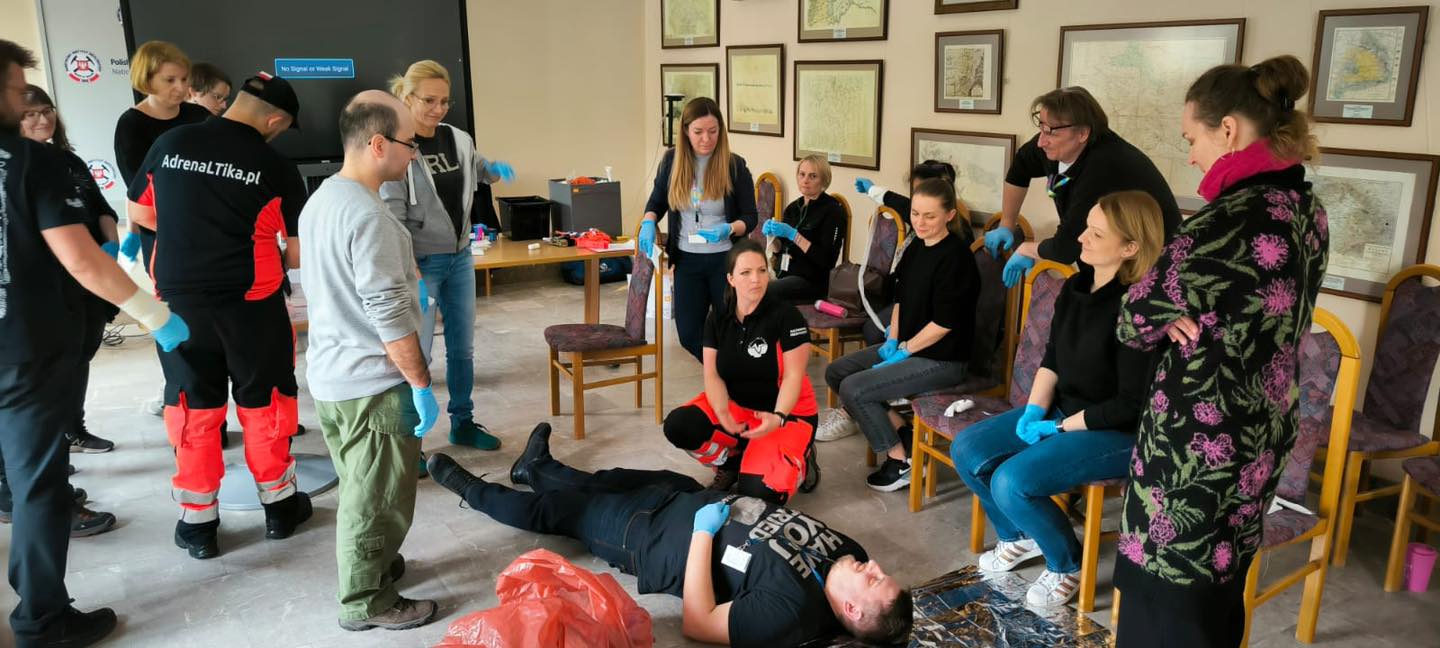 grupa osób w sali ćwiczy udzielanie pierwszej pomocy osobie poszkodowanej
