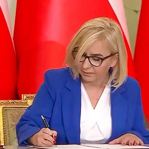 Ministra podpisujaca dokument na tle flagi Polski