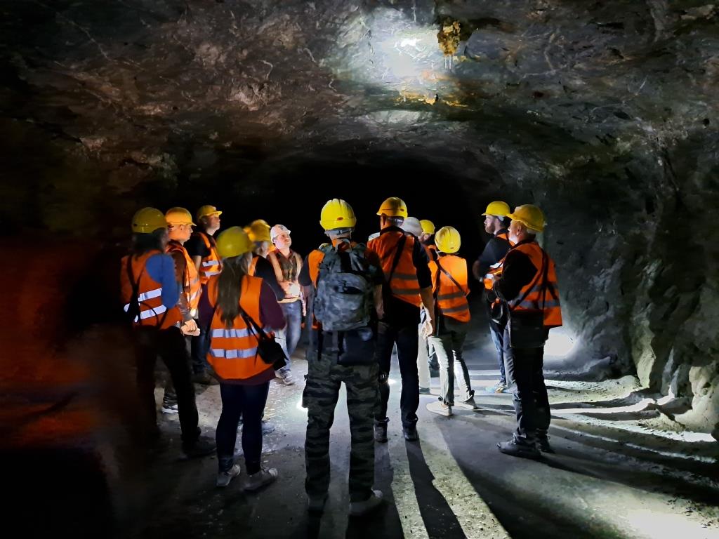 wnętrze kopalni soli, w wyrobisku stoi grupa osób w żółtych kaskach i kamizelkach odblaskowych