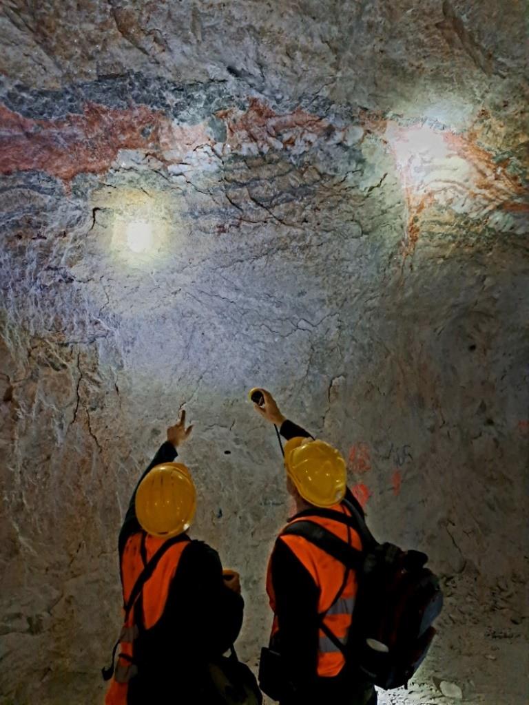 wnętrze kopalni soli, przed ścianą wyrobiska stoją tyłem dwie osoby i pokazują sobie ciekawe struktury solne