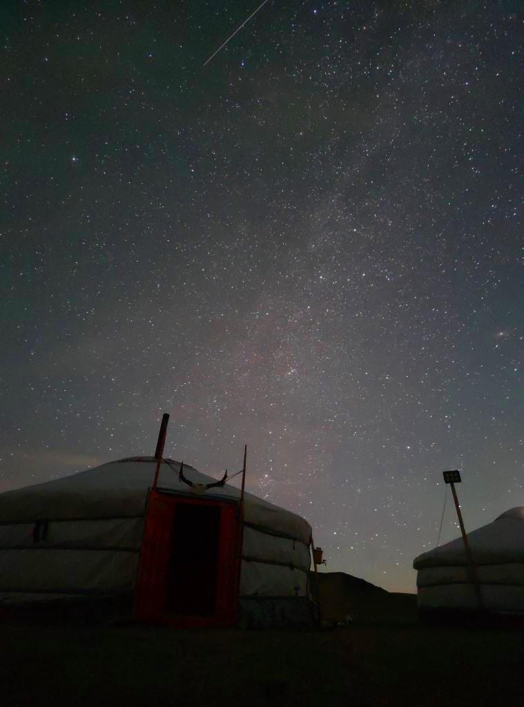 rozgwieżdżone nocne niebo i spadająca gwiazda, w dole namiot jurta