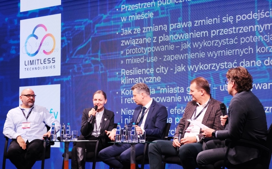 kilka osób siedzi na krzesłach i rozmawia na tle dużego baneru