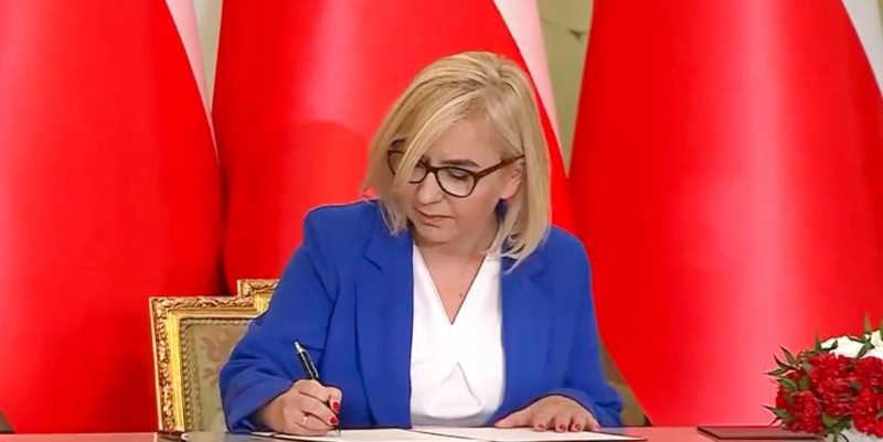 Ministra podpisujaca dokument na tle flagi