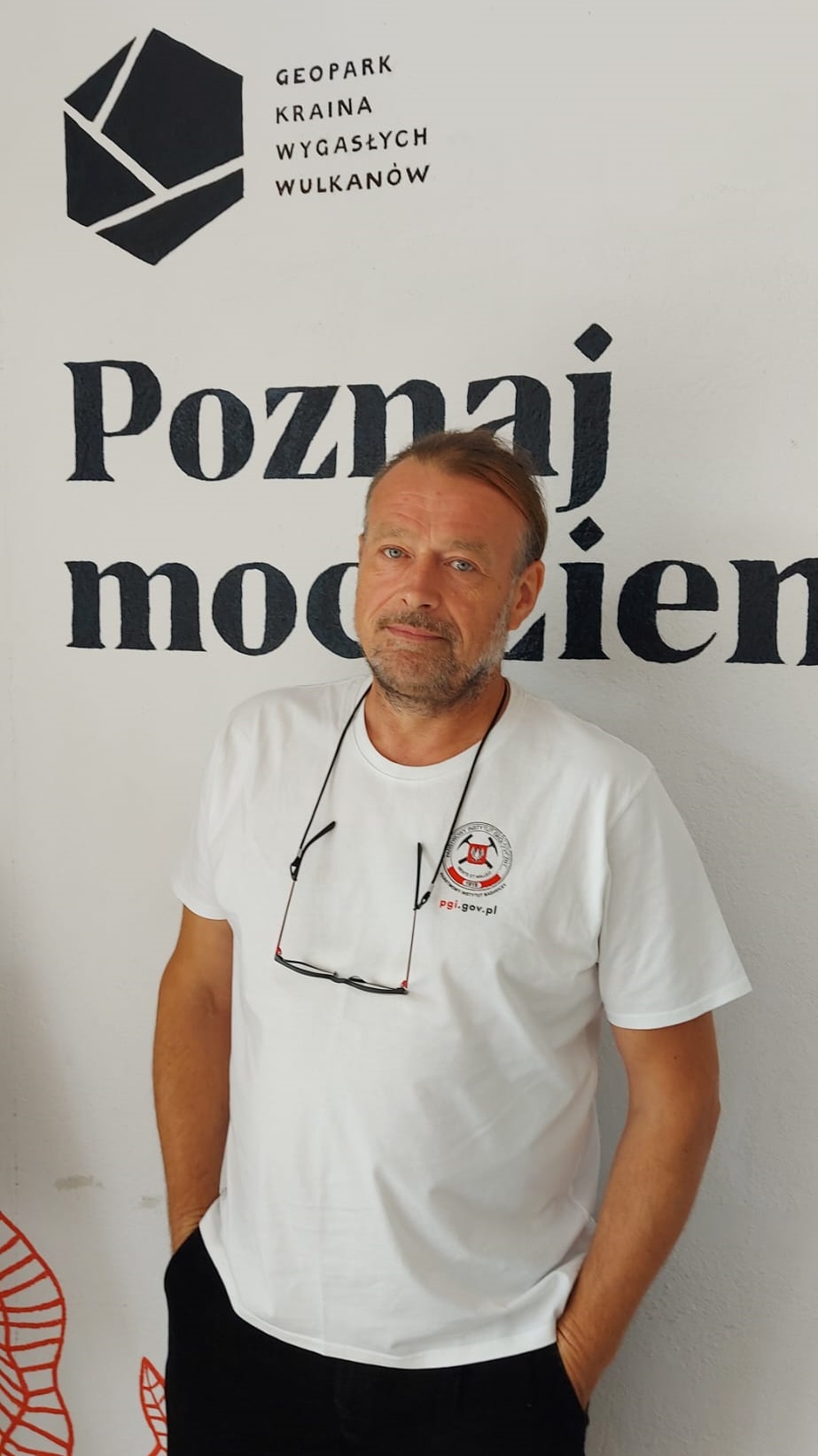 mężczyzna pozuje do zdjęcia na tle ściany z logo