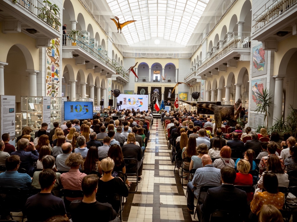 dużo osób siedzących na krzesłach w sali muzealnej podczas uroczystej sesji
