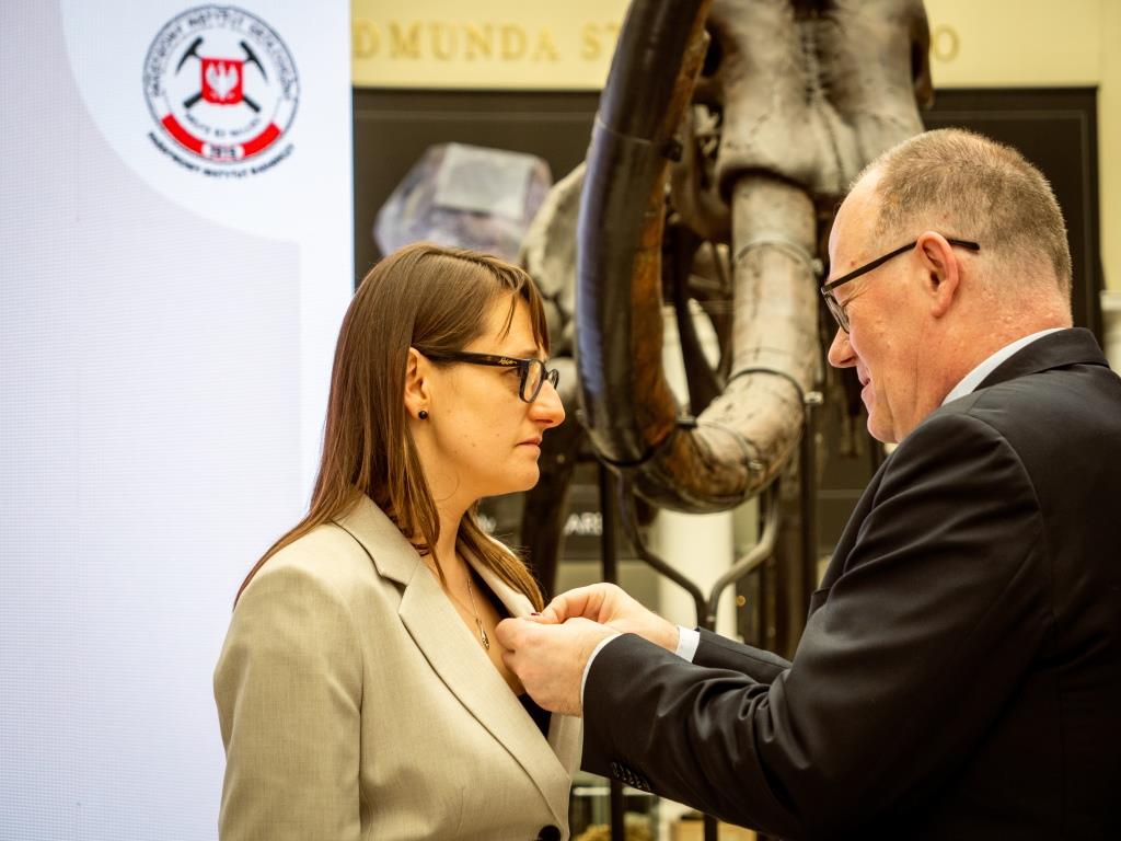 mężczyzna w garniturze przypina kobiecie medal