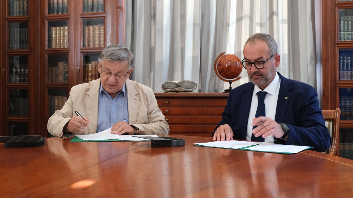 dwóch mężczyzn podpisuje umowę siedząc przy stole w pięknej bibliotece