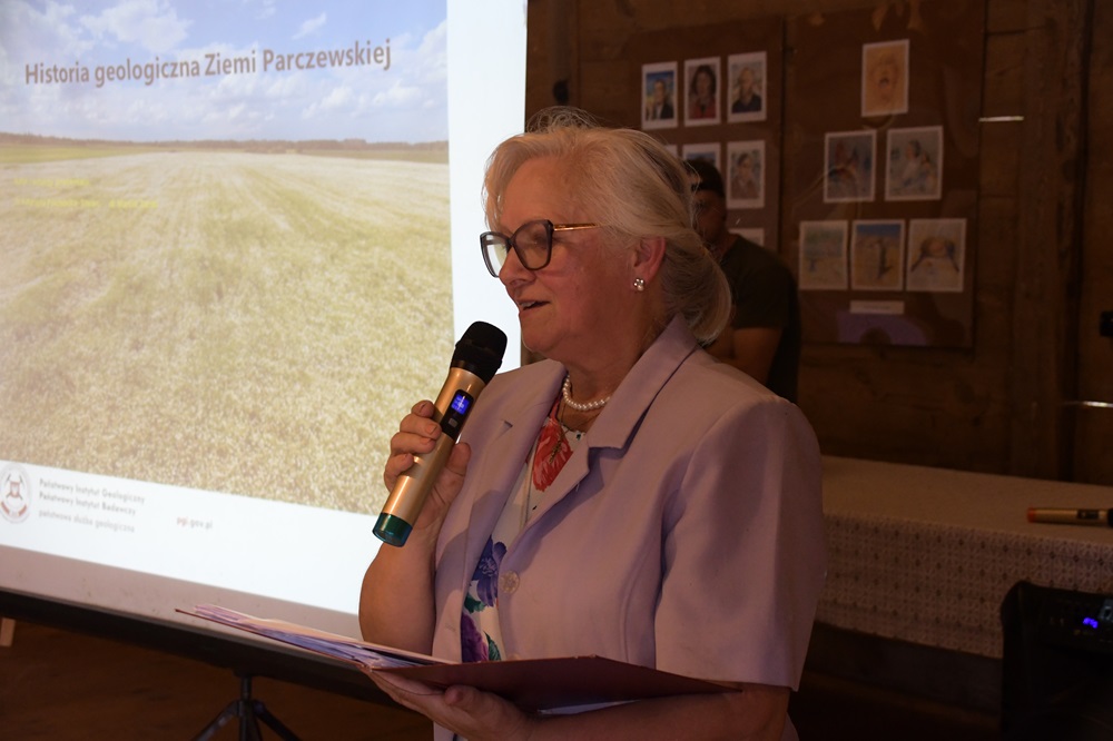 kobieta z mikrofonem w dłoni na tle ekranu z prezentacją