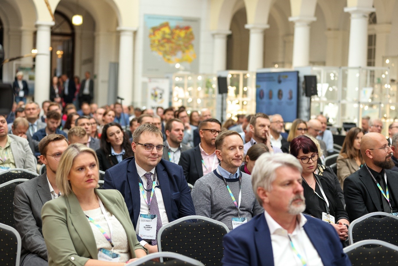 sala muzealna wypełniona ludźmi - słuchaczami konferencji siedzącymi na krzesłach