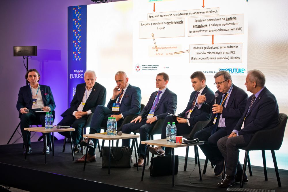 kilku mężczyzn w garniturach bierze udział w dyskusji panelowej w dużej skali
