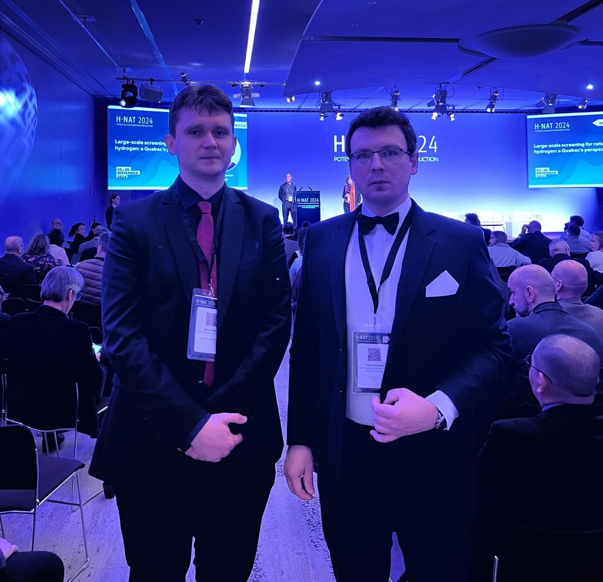 dwóch mężczyzn pozujących do zdjęcia w sali konferencyjnej wypełnionej słuchaczami