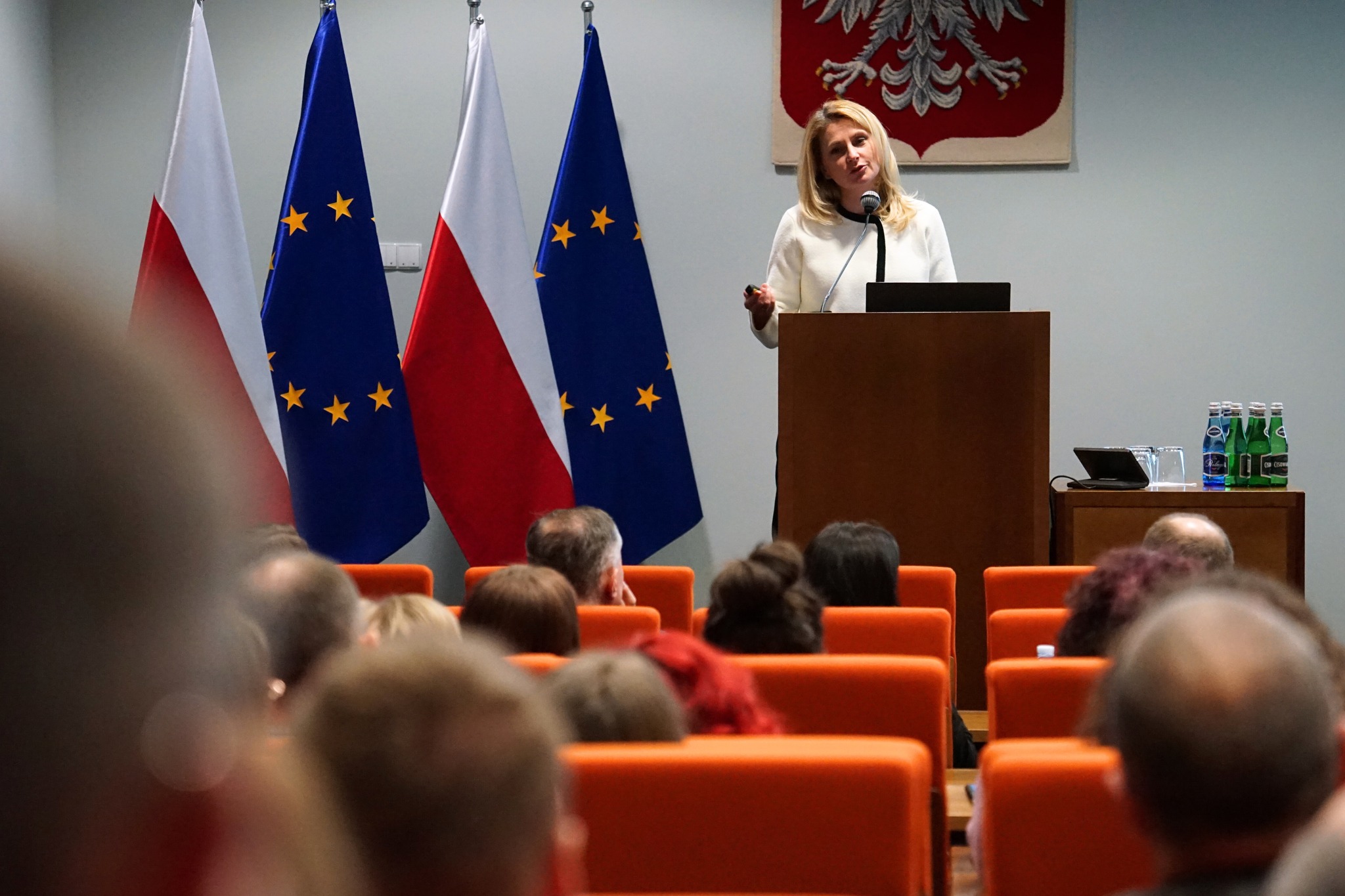 kobieta stojąca przy pulpicie i referująca prezentację wyświetlona na ekranie