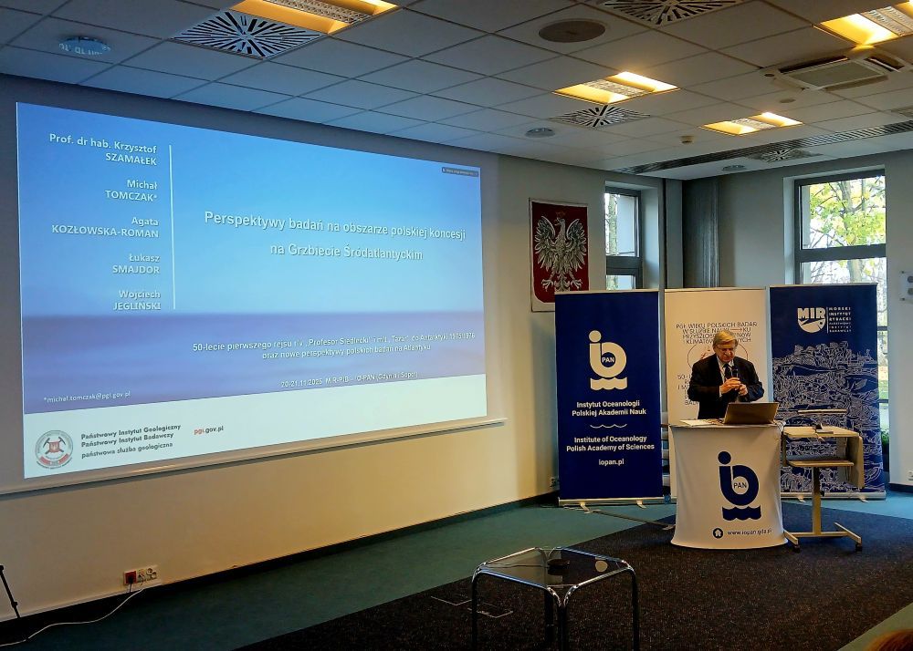 mężczyzna z mikrofonem w ręce podczas prelekcji, na tle ekranu