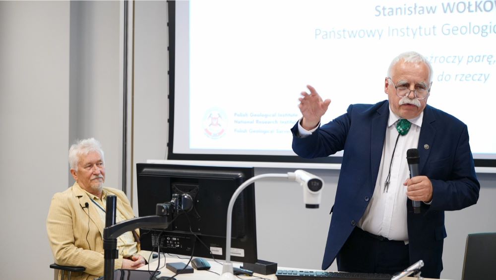 mężczyzna z mikrofonem w ręce podczas prelekcji, na tle ekranu