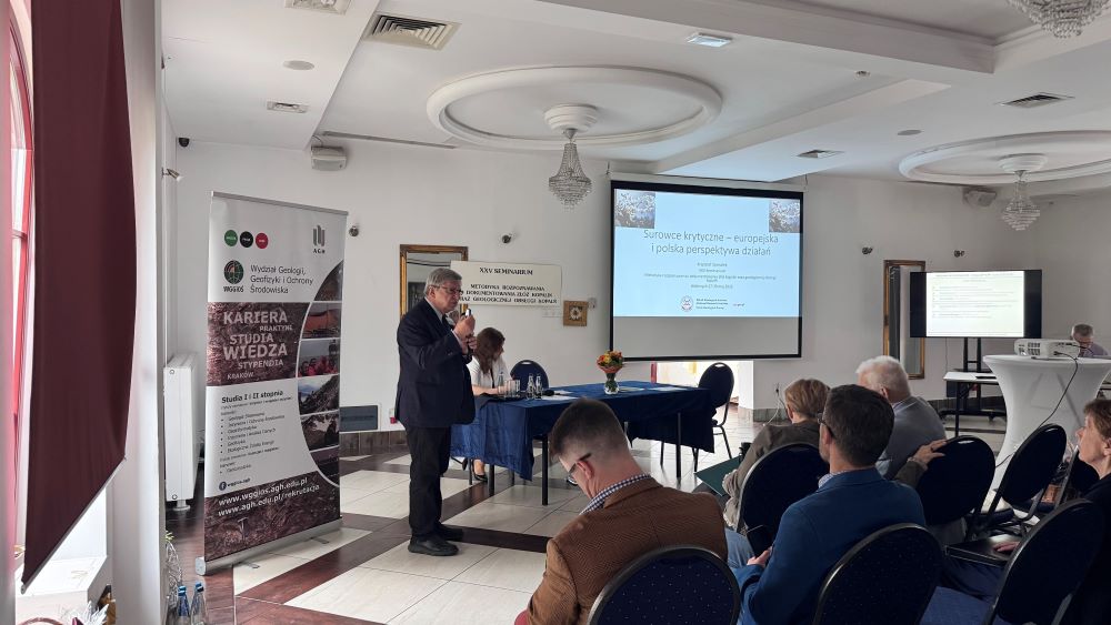 mężczyzna z mikrofonem w ręce podczas prelekcji, na tle ekranu