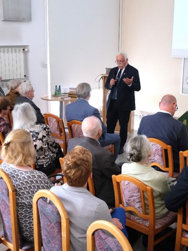mężczyzna z mikrofonem w ręce podczas prelekcji, na tle ekranu