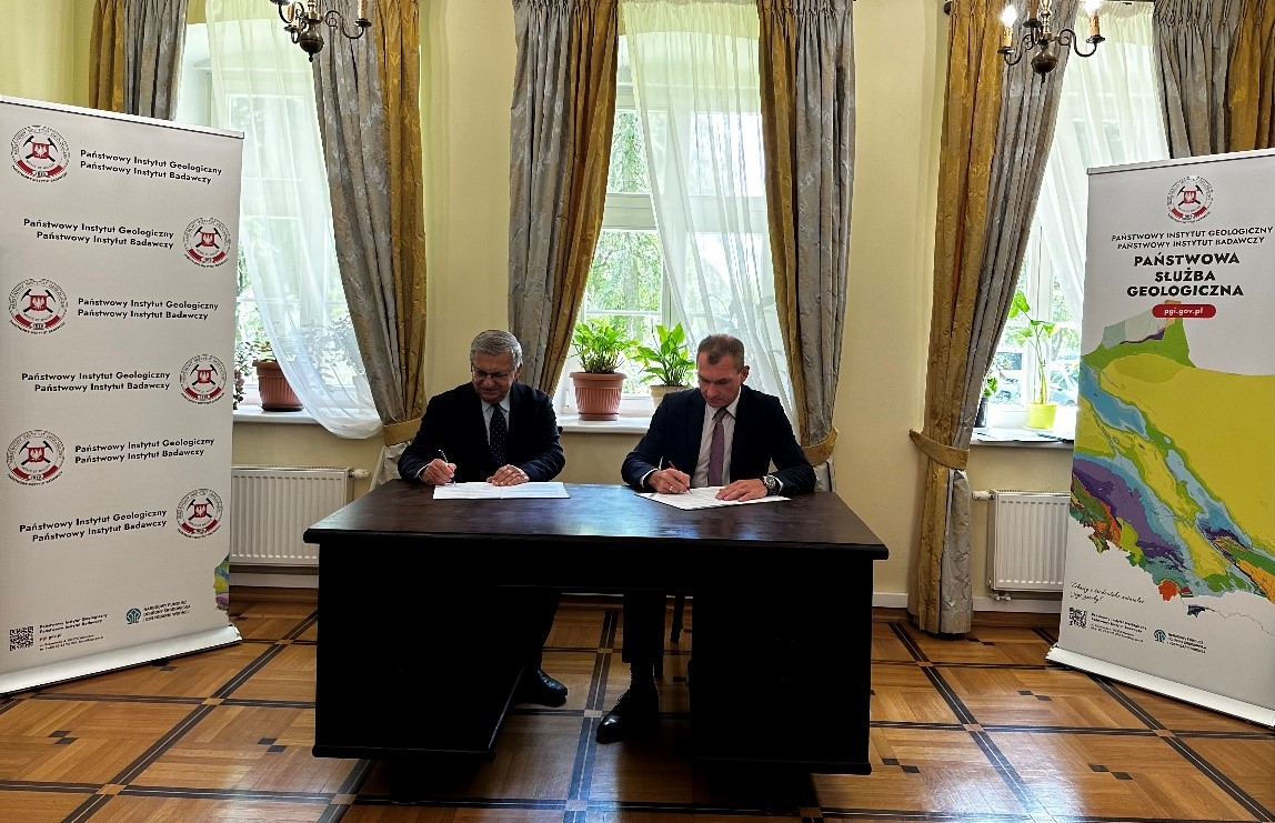 dwóch mężczyzn siedzi przy stole i podpisuje umowy