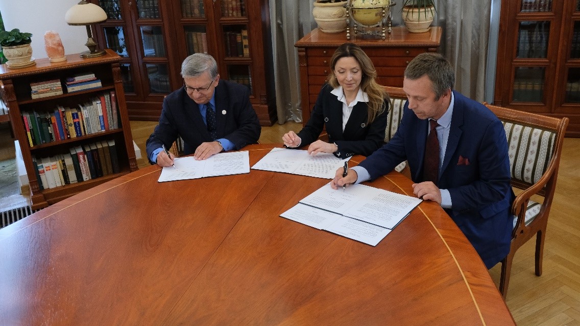 troje ludzi podpisuje dokument siedząc przy stole