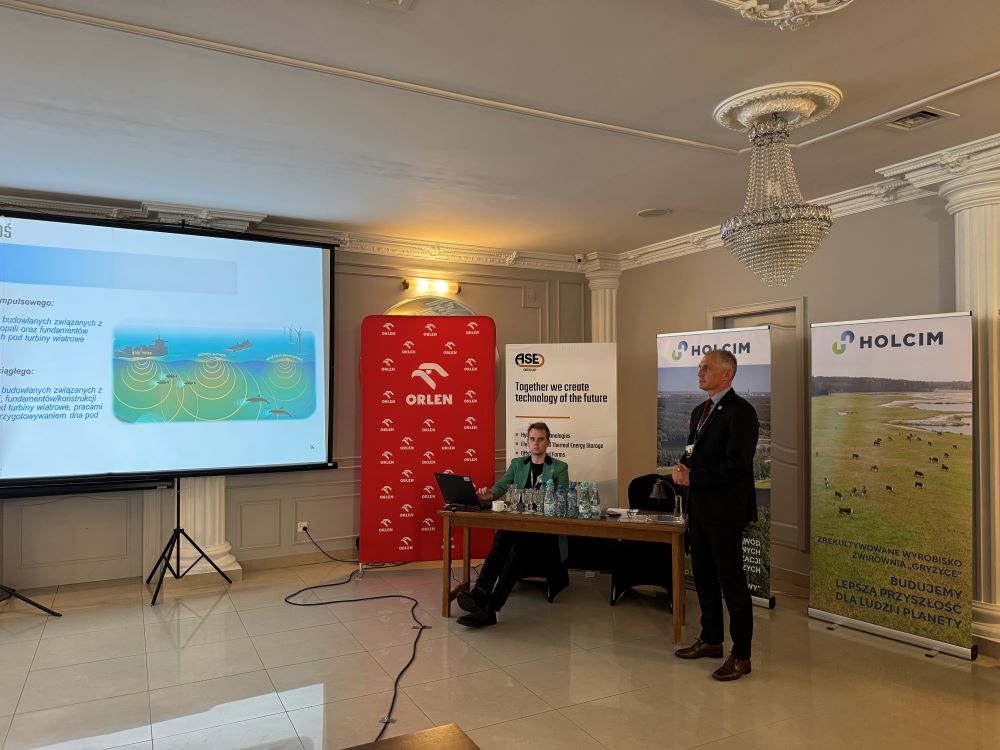 mężczyzna przemawia do siedzącej w pomieszczeniu publiczności