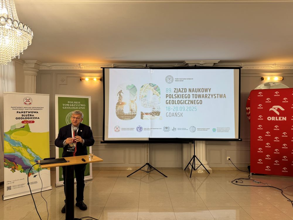 mężczyzna z mikrofonem w ręce podczas prelekcji, na tle ekranu