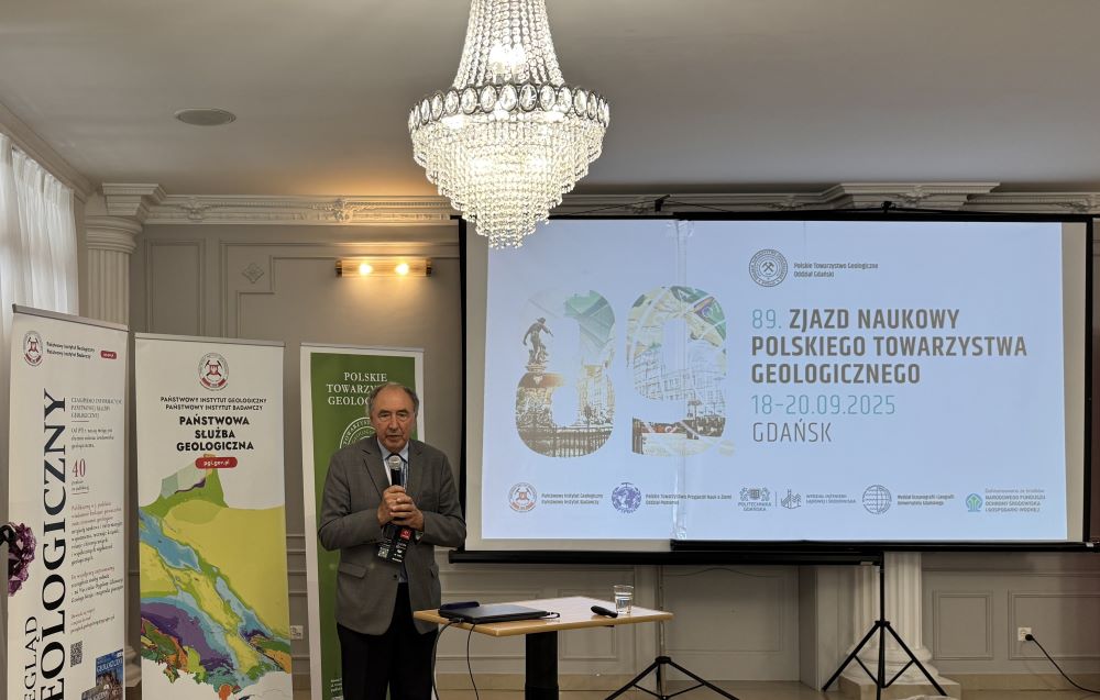 mężczyzna z mikrofonem w ręce podczas prelekcji, na tle ekranu