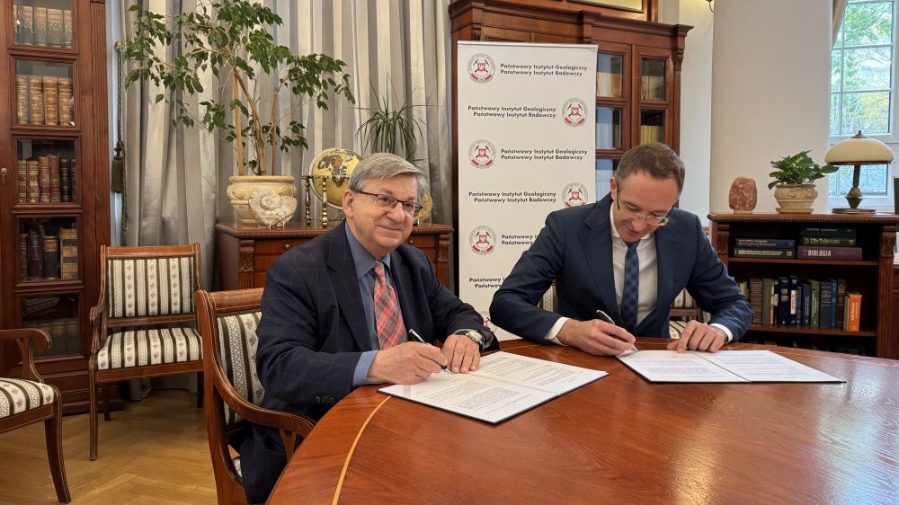 dwóch mężczyzn podpisuje umowę siedząc przy stole