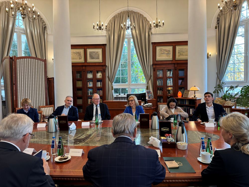 grupa osób siedząca na sali przy stole i prowadzących rozmowę ze sobą