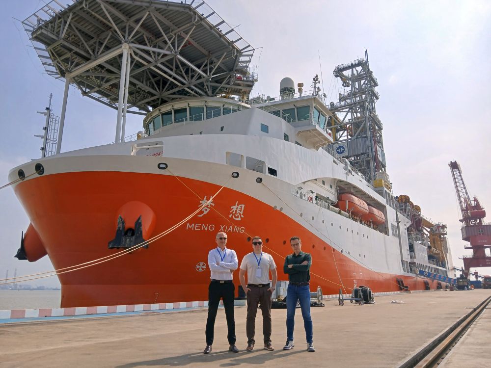 trzech mężczyzn pozuje do zdjęcia na tle statku badawczego