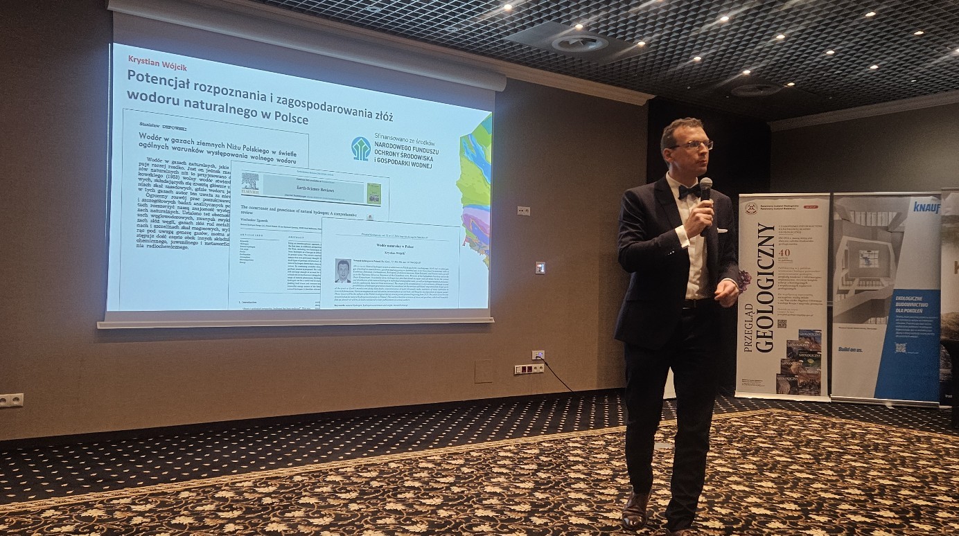 mężczyzna z mikrofonem w ręce podczas prelekcji, na tle ekranu