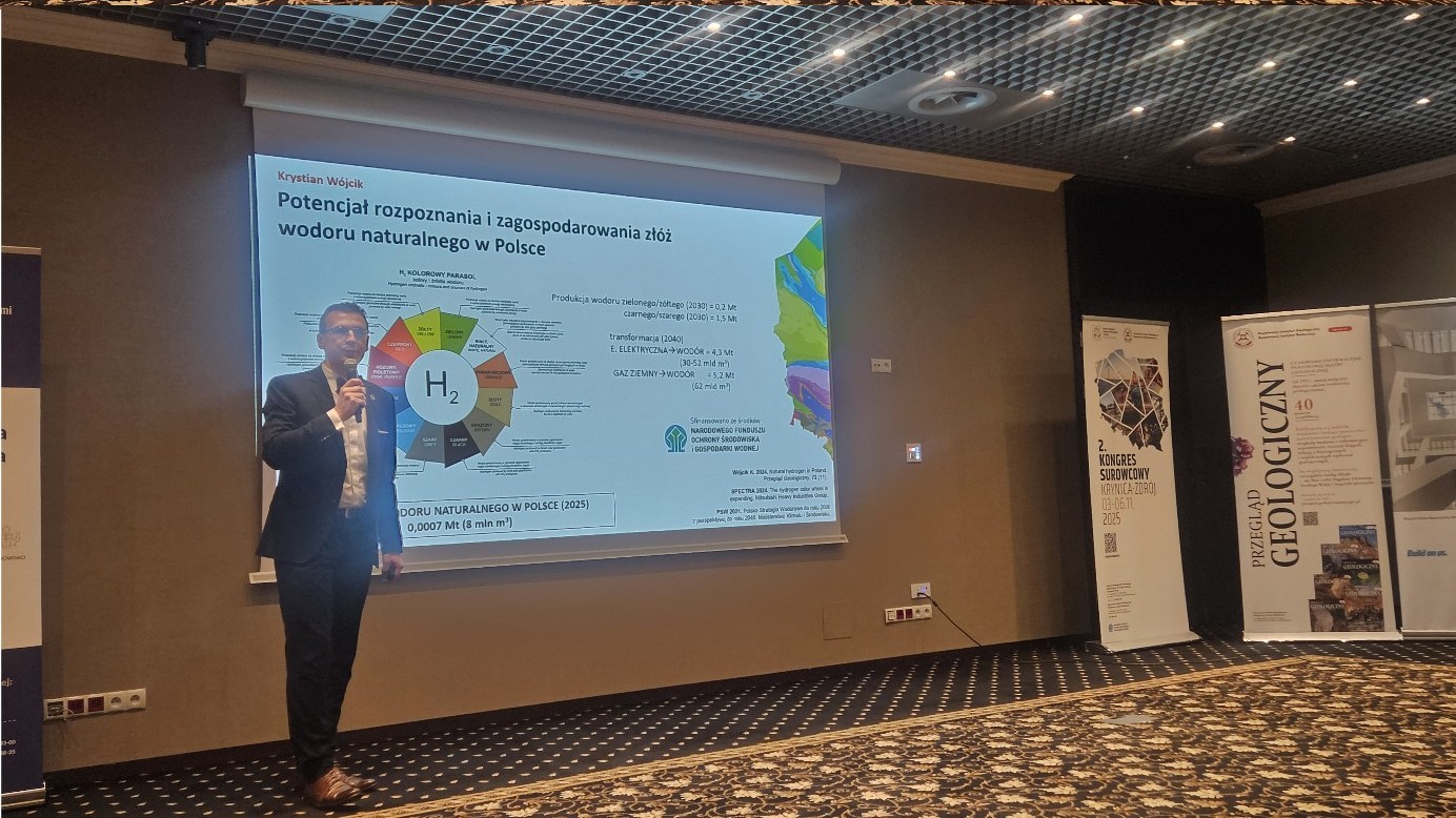 mężczyzna z mikrofonem w ręce podczas prelekcji, na tle ekranu