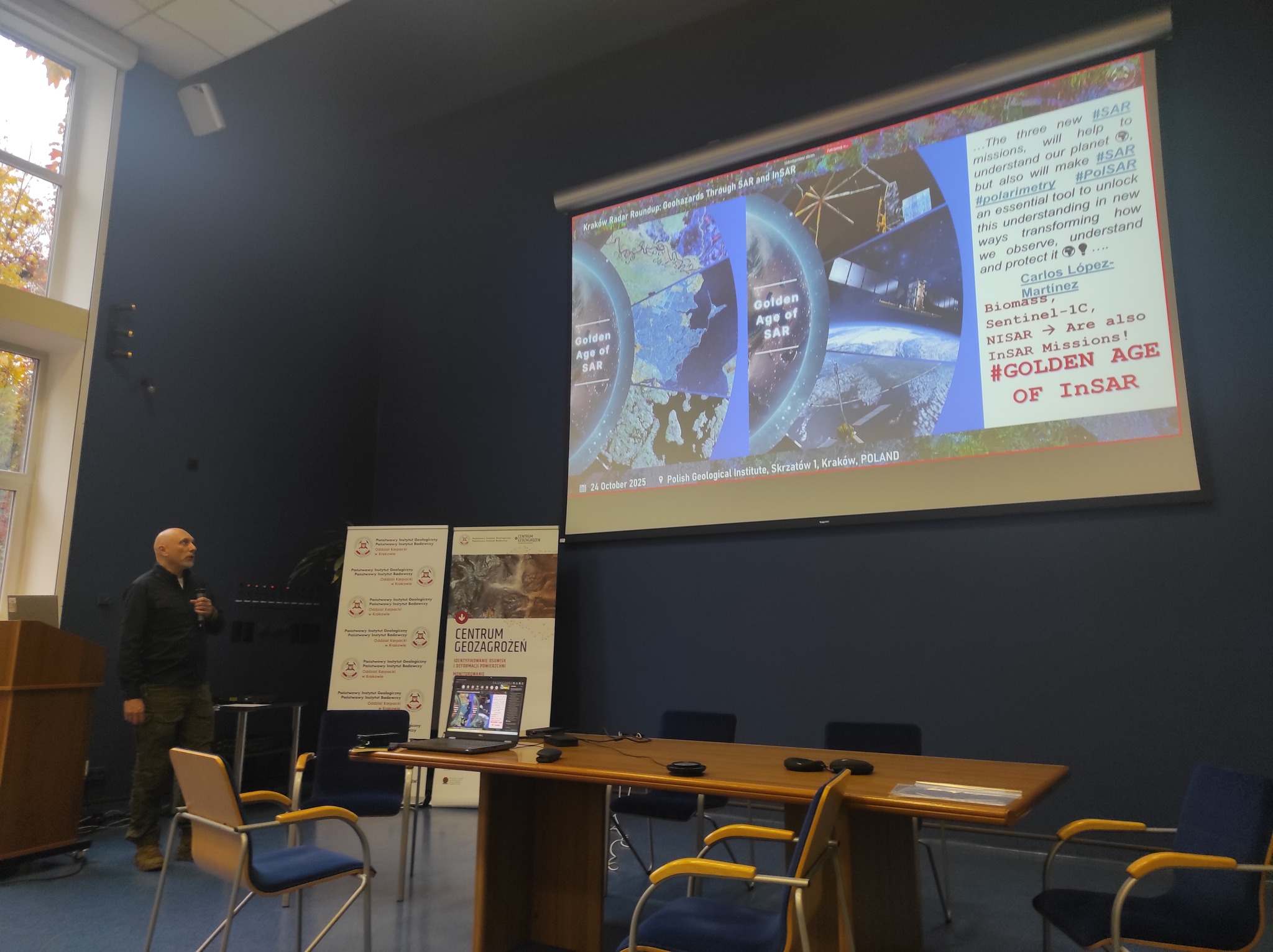 mężczyzna z mikrofonem w ręce podczas prelekcji, na tle ekranu