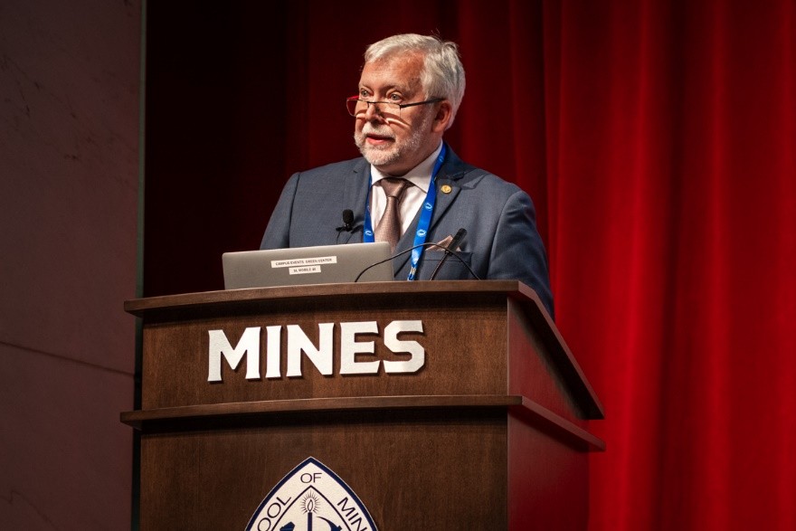 mężczyzna przemawia do siedzącej w pomieszczeniu publiczności