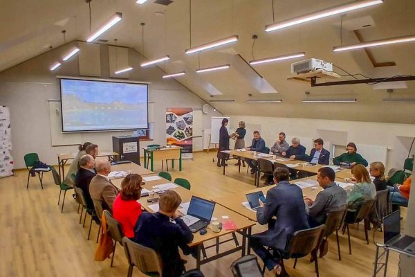 grupa osób siedząca na sali przy stole i prowadzących rozmowę ze sobą