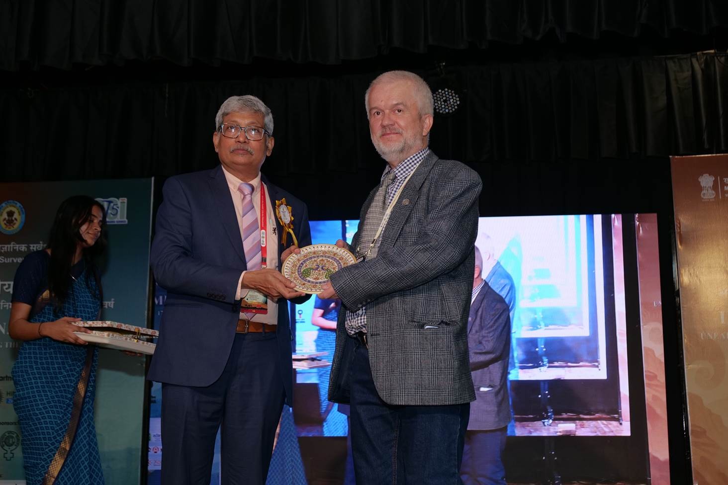 dwóch mężczyzn na scenie jeden wręcza drugiemu prezent