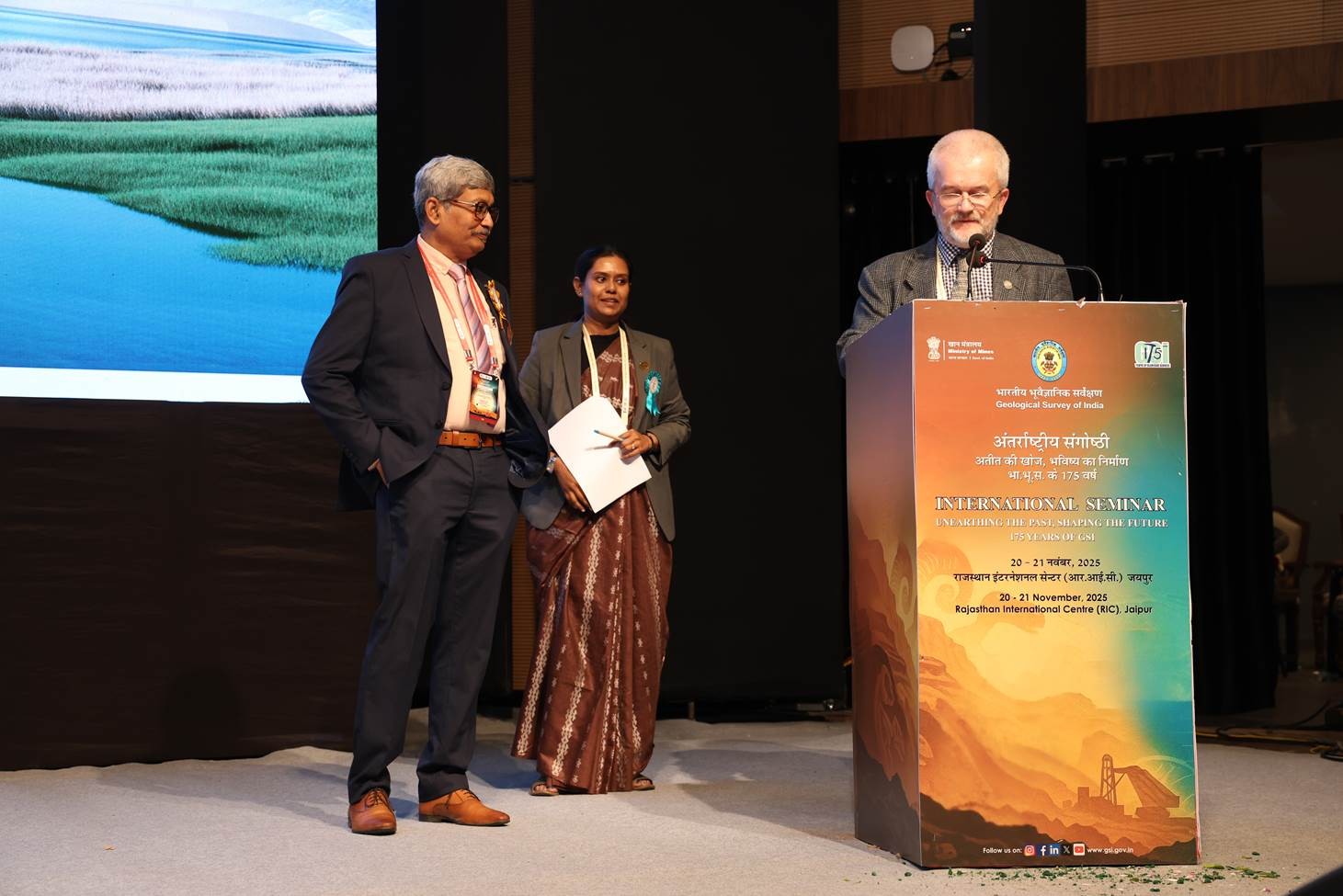 mężczyzna z mikrofonem w ręce podczas prelekcji, na tle ekranu