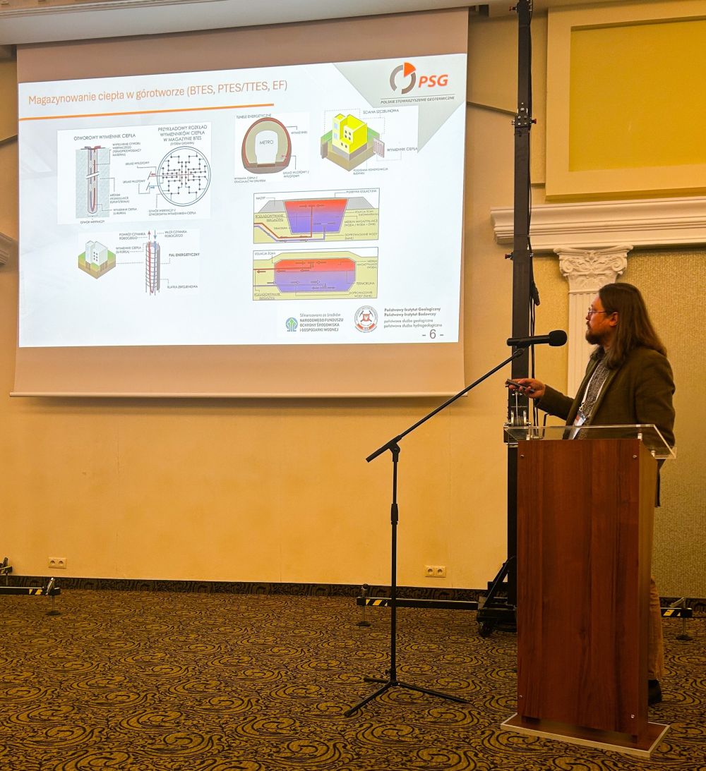 mężczyzna z mikrofonem w ręce podczas prelekcji, na tle ekranu