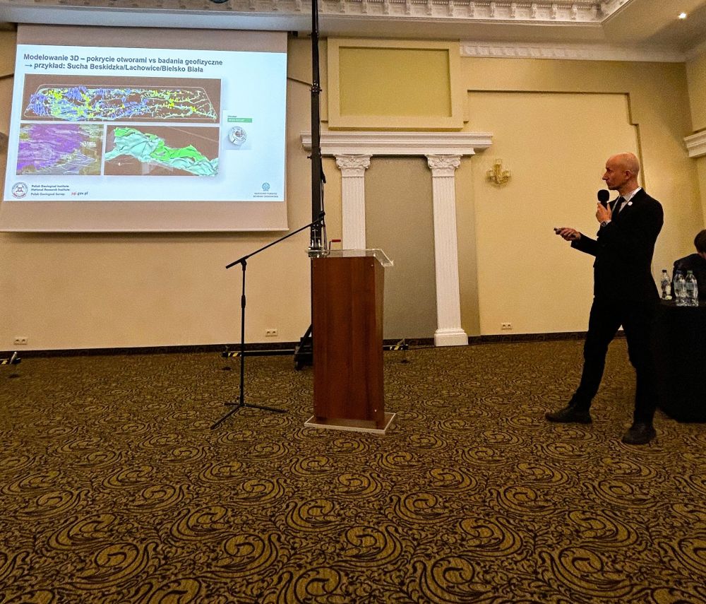 mężczyzna z mikrofonem w ręce podczas prelekcji, na tle ekranu