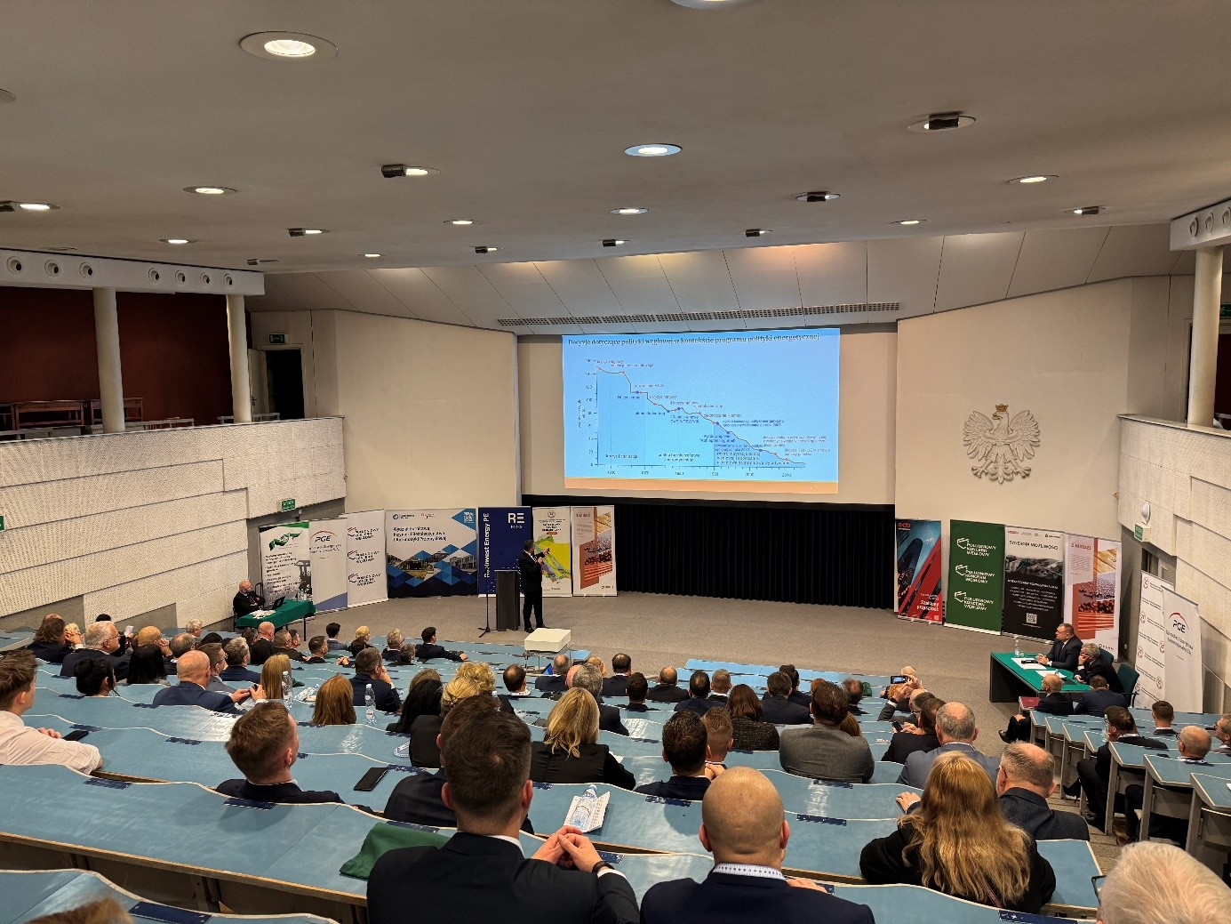 mężczyzna z mikrofonem w ręce podczas prelekcji, na tle ekranu