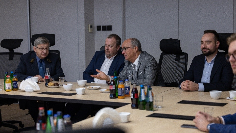 grupa osób siedząca na sali przy stole i prowadzących rozmowę ze sobą