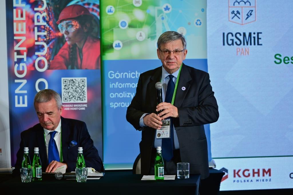 mężczyzna w garniturze trzyma mikrofon w ręku i przemawia do słuchaczy
