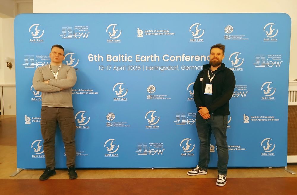 dwóch mężczyzn pozuje do zdjęcia na tle ścianki reklamowej konferencji