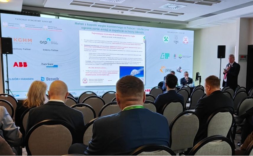 mężczyzna z mikrofonem w ręce podczas prelekcji, na tle ekranu