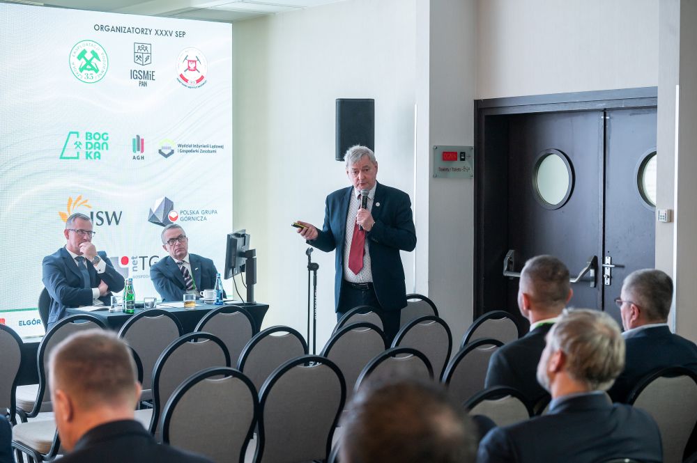 mężczyzna z mikrofonem w ręce podczas prelekcji, na tle ekranu