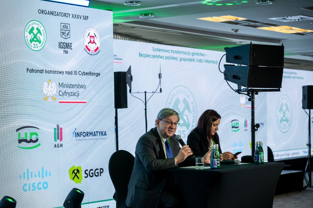 mężczyzna z mikrofonem w ręce podczas prelekcji, na tle ekranu